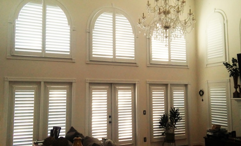 TV room in two-story Bakersfield house with plantation shutters on arch windows.