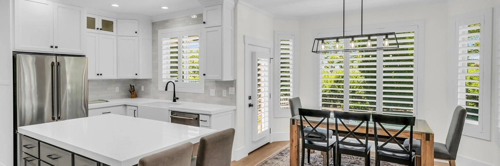 White plantation shutters on different-sized windows in a kitchen and dining room